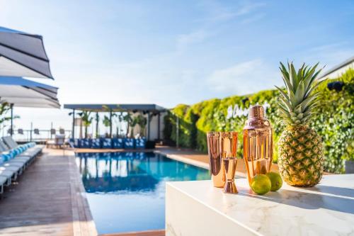 a table with a pineapple and two glasses next to a pool at Sofitel Barcelona Skipper in Barcelona
