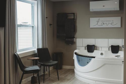 a bathroom with a tub and two chairs and a window at Riverside Suites in Grand Falls -Windsor