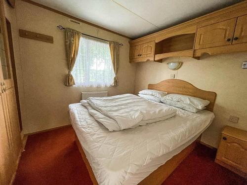 a small bedroom with a bed with white sheets at Superb Caravan With Decking At Southview Holiday Park Ref 33093s in Skegness