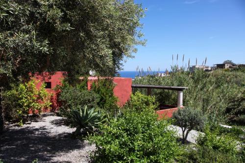 a garden with a red house and trees and the ocean at Residence Salina in Malfa