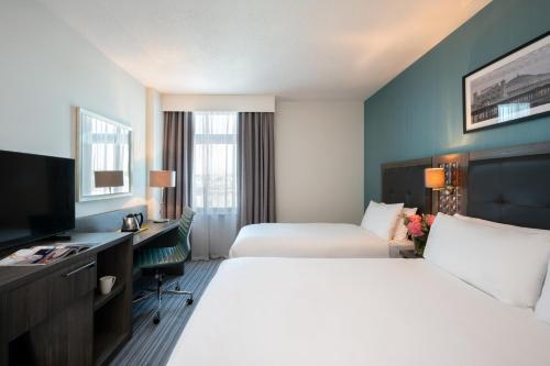 a hotel room with two beds and a desk and a television at Leonardo Hotel Brighton in Brighton & Hove