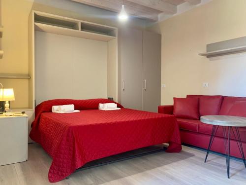 a bedroom with a red bed and a couch at Monolocale con giardino a 100m dal mare Punta Ala in Punta Ala