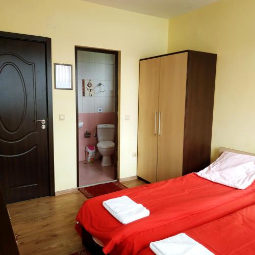 a bedroom with a bed with red sheets and a toilet at Къща за гости СИАНА in Dospat