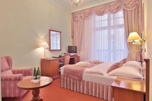 a hotel room with a bed and a chair and a window at Olympia Wellness Hotel in Karlovy Vary