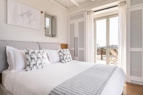 a white bedroom with a large bed and a balcony at Villa Olivia Mykonos in Agios Stefanos