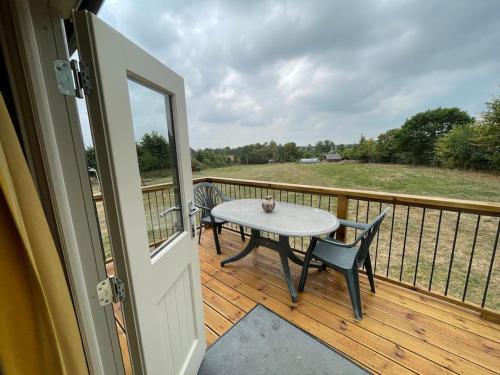 a porch with a table and chairs on a deck at The Old Post Office - Luxurious Shepherds Hut 'Far From the Madding Crowd' based in rural Dorset. in Todber