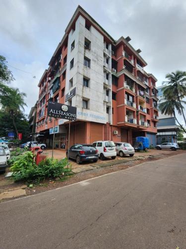 duży budynek apartamentowy z samochodami zaparkowanymi przed nim w obiekcie All Seasons Guest House I Rooms & Dorms w mieście Margao