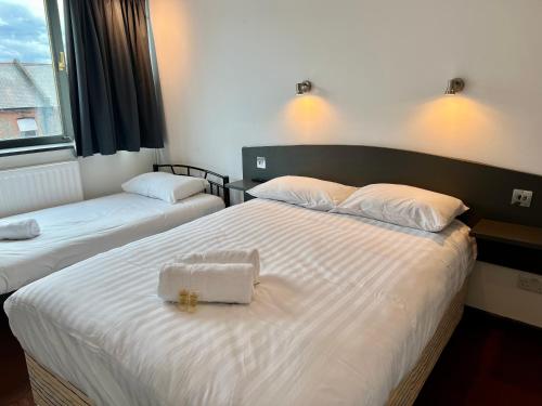 a bedroom with two beds with white sheets and a bag on it at Hounslow Central Hotel in Hounslow