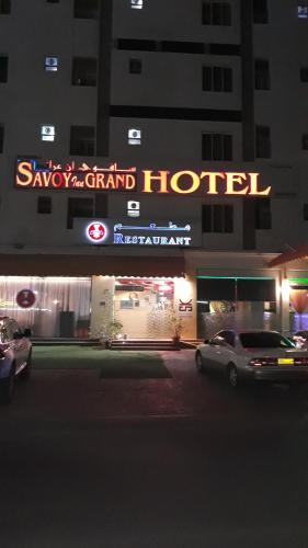 a sign for a hotel with cars parked in front of it at Savoy Grand Hotel Apartments in Muscat