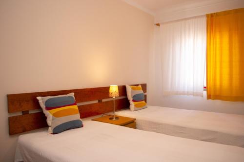 a bedroom with two beds with a lamp and a window at Apartamentos Monte da Rosa in Vila Nova de Milfontes