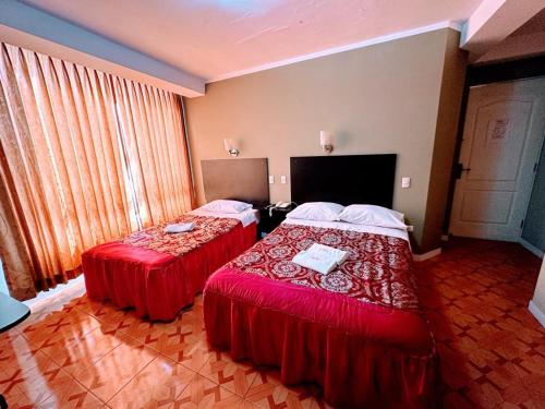 two beds in a hotel room with red sheets at HOTEL CASA REAL in Tacna