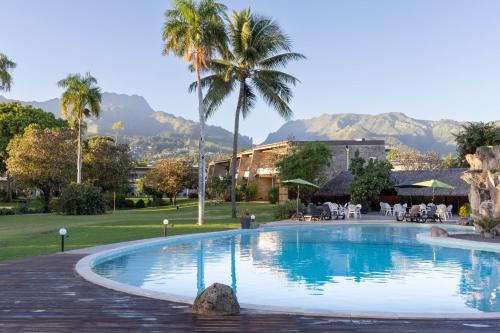 a swimming pool with palm trees and mountains in the background at Royal Tahitien in Papeete