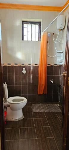 a bathroom with a toilet and an orange shower curtain at Betty Homes in Mombasa