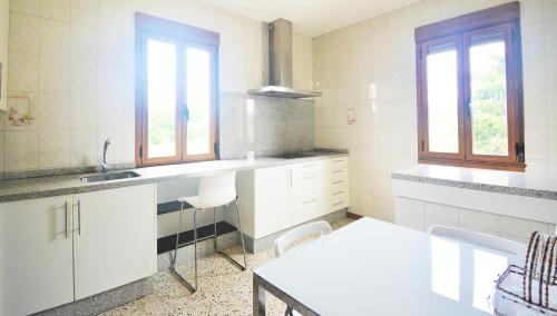 eine Küche mit weißen Schränken, einem Waschbecken und 2 Fenstern in der Unterkunft GALIHOST - Casa con jardín en Cambados in Cambados
