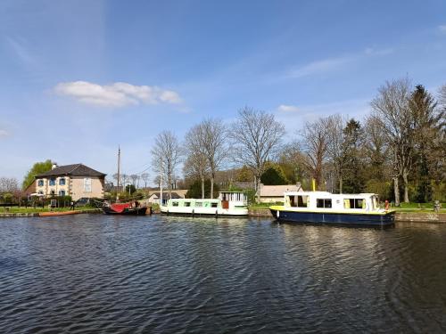 three boats are docked on the water near a house at Ille Flottante, Maison éclusière et hébergements insolites sur le canal in Hédé