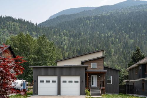 a house with two garage doors in front of a mountain at Mountain Dreams - Revelstoke Home Near RMR in Revelstoke