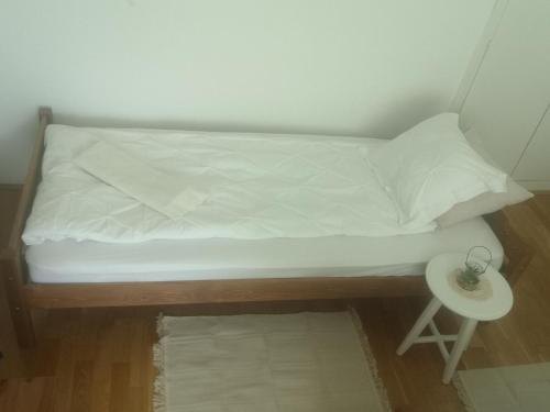 uma pequena cama com lençóis brancos e uma mesa lateral em Antik Apartman em Veszprém