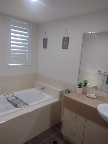Baño blanco con bañera y lavamanos en Ocean Breeze Apartments, en Hervey Bay