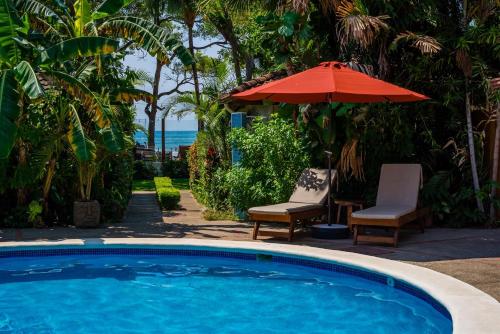 a swimming pool with an umbrella and two chairs and a table at The Coast Beachfront Hotel in Tamarindo