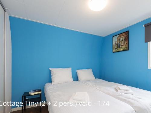 a blue bedroom with a bed with white sheets at Beautiful cottage with dishwasher, in a holiday park not far from Giethoorn in De Bult