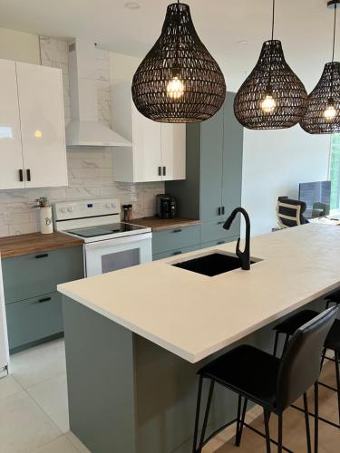 a kitchen with white cabinets and a sink and lights at Appartement Le Yin in Sainte-Anne-de-Beaupré
