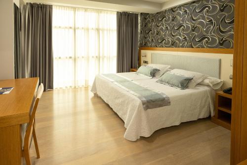 a bedroom with a large bed and a table and a desk at Hotel Montedobra in Torrelavega