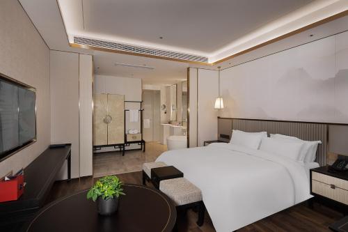 Hangzhou Junsun Luxury Hotel في هانغتشو: غرفة نوم بسرير ابيض كبير وطاولة