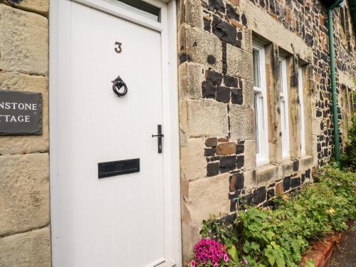 a white door on a brick house with flowers at Whinstone Bamburgh in Bamburgh
