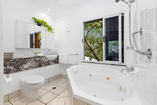 a bathroom with a tub and a toilet and a window at Palm Cove Treetop Spa Retreat in Palm Cove