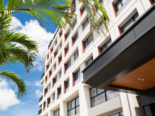 a facade of a building with palm trees at REF Okinawa Arena by VESSEL HOTELS in Okinawa City