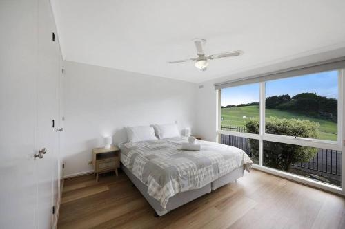 a white bedroom with a bed and a large window at Logans Beach Apartments - Greenviews in Warrnambool