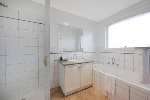 Baño blanco con bañera y lavamanos en Logans Beach Apartments - Greenviews en Warrnambool