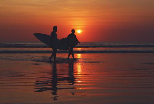 two people walking on the beach at sunset with their surfboards at KUTA - 4BR Villa with Private XL Pool in Kuta