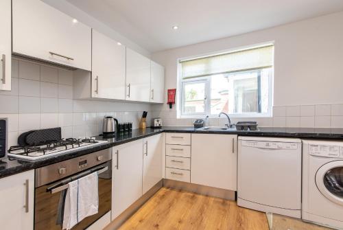 Una cocina con gabinetes blancos y lavadora y secadora. en Gertrude House - Spacious 3BR Bungalow in Nottingham, en Nottingham
