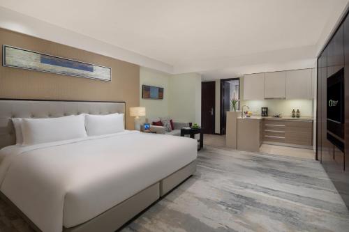 a bedroom with a large white bed and a kitchen at Oakwood Residence Hangzhou in Hangzhou