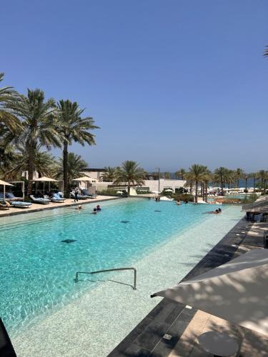 a large swimming pool with palm trees and people in it at The Address Residence Fujairah in Fujairah