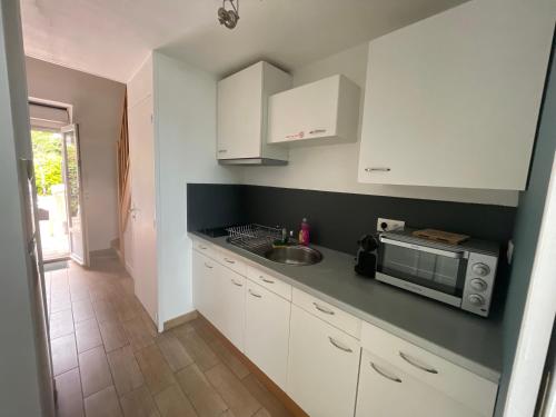 une cuisine avec des armoires blanches, un évier et un micro-ondes dans l'établissement Duplex au calme jardinet Spa, à Plescop