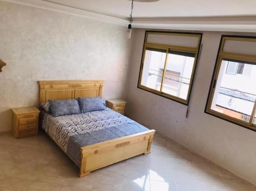 a bedroom with a wooden bed and two windows at Charmant appartement in Al Hoceïma