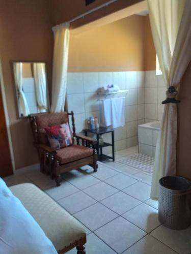 uma casa de banho com uma banheira, uma cadeira e uma banheira. em Kwa-Dlamathe Guesthouse em Volksrust