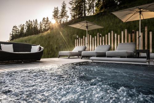 a hot tub with chairs and umbrellas on a wooden deck at Hotel Schmung in Alpe di Siusi