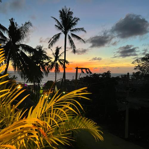 a sunset with palm trees in front of the ocean at Oceanview Bungalows by EAT in Karon Beach