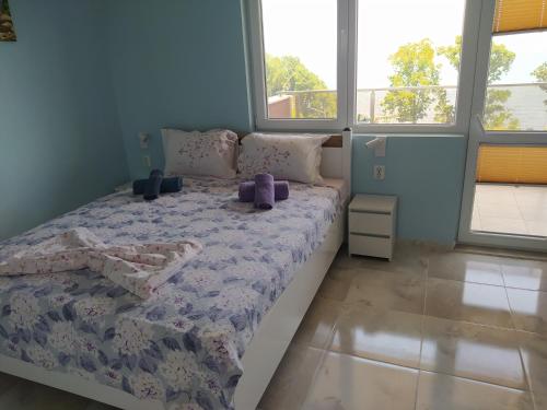 a bedroom with a bed with a purple comforter and windows at Апартамент White apartment град Китен in Kiten