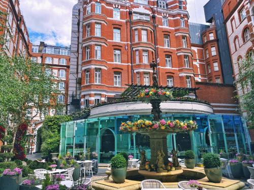 a building with a fountain with flowers in front of it at St. James' Court, A Taj Hotel, London in London