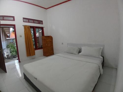 Cama blanca en habitación blanca con ventana en Roby Homestay en Kuta Lombok