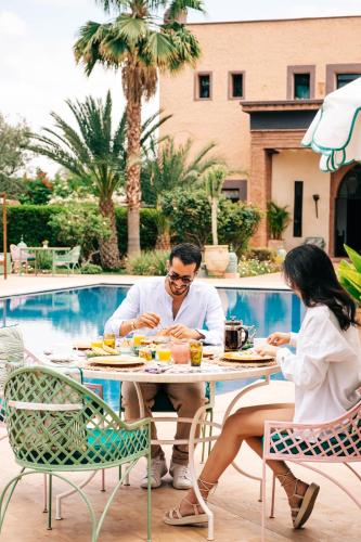 a man and woman sitting at a table by a pool at La Villa Des Golfs & PinkCactus in Marrakesh
