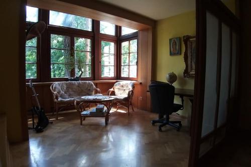 a living room with two chairs and a table and windows at Leśny kasztel pod sosnami. Pokój w koronach drzew. in Milanówek