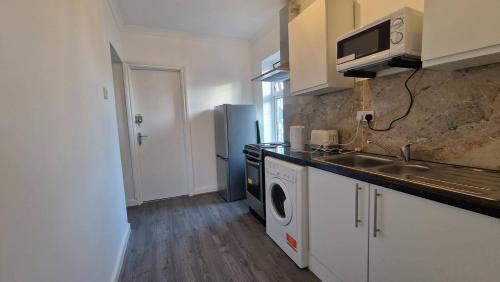 Captivating 2-Bed Apartment in Ilford في إلفورد: مطبخ مع مغسلة وغسالة ملابس