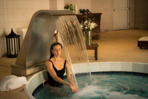 a woman sitting in a swimming pool with a waterfall at Carilo Village Apart Hotel & Spa in Carilo