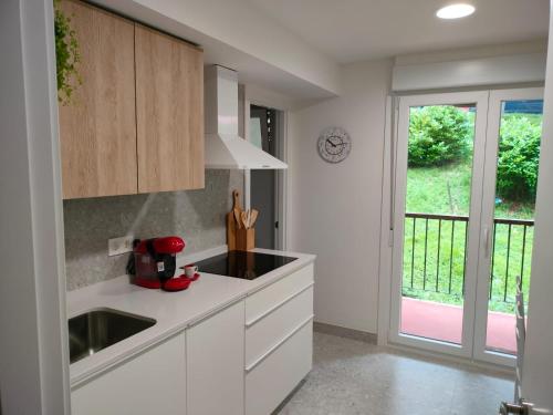 d'une cuisine avec des placards blancs, un évier et une fenêtre. dans l'établissement Apartamento familiar con vistas a la montaña en Zarautz, à Zarautz