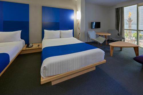 a hotel room with two beds and a table and chairs at City Express Plus by Marriott Ciudad de México Reforma El Ángel in Mexico City